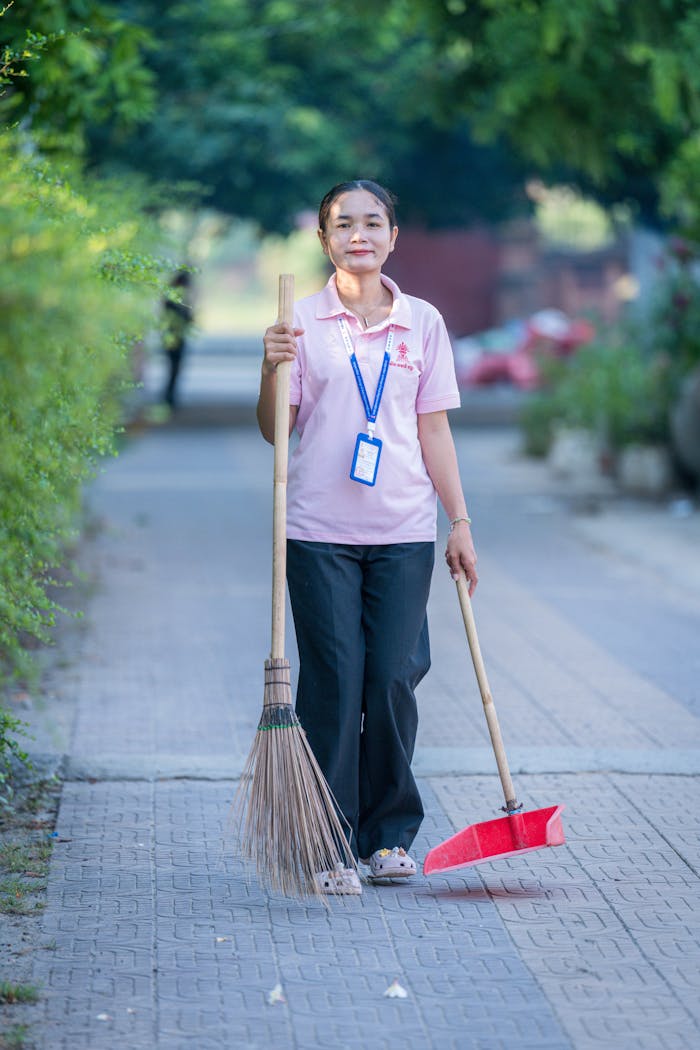 Portrait of a female street cleaner holding a broom and dustpan in Krong Battambang, Cambodia.