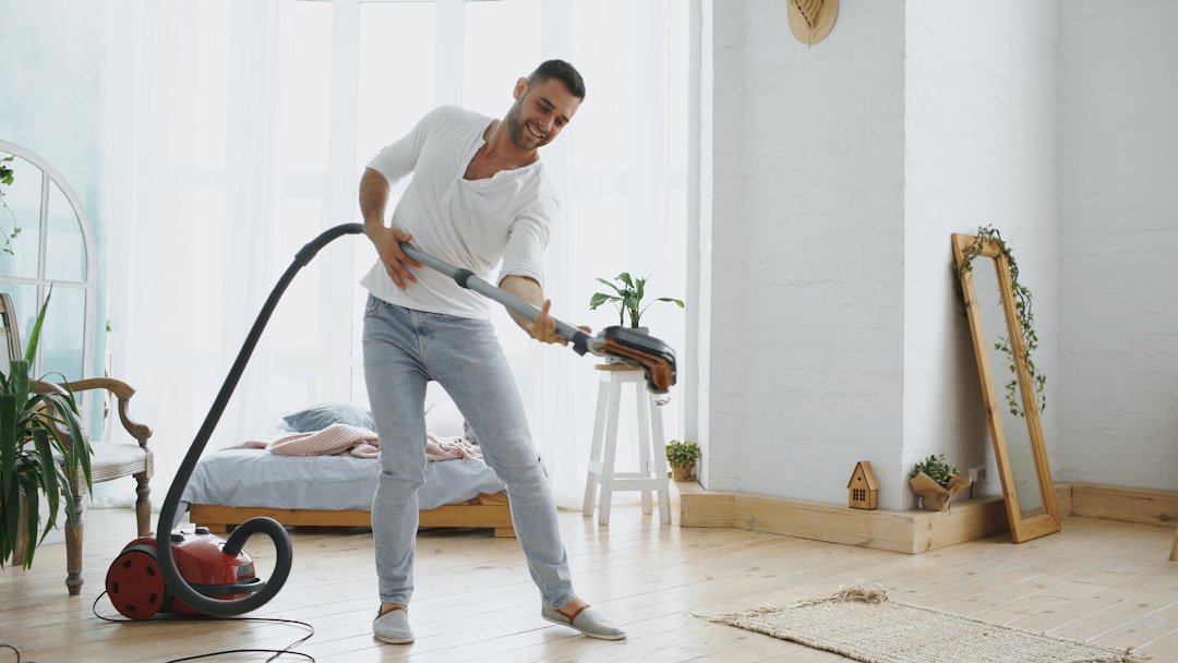 Dancing young man having fun cleaning house with vacuum cleaner at home