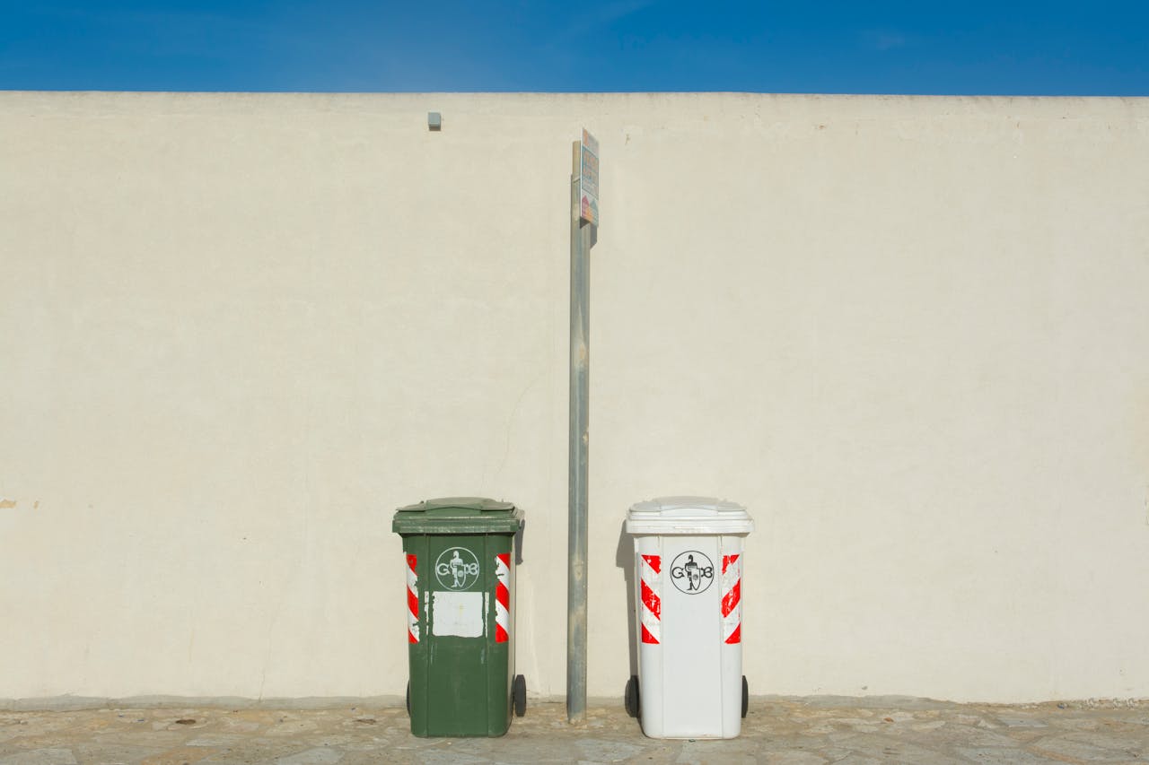 services-06 Two recycling bins next to a white wall under a clear blue sky, capturing urban simplicity.